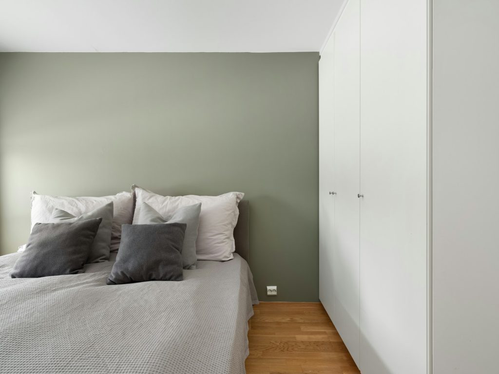 Bedroom with soft green painted walls and a white bed, illustrating a calm herbal green like Celery