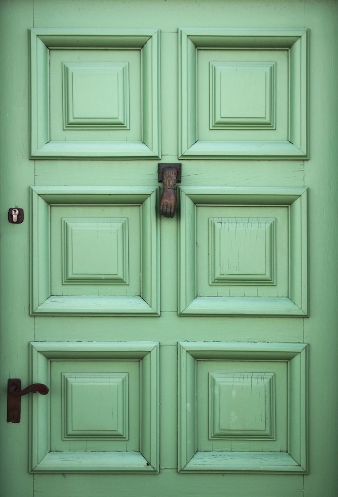 Paneled front door painted a soft green with a dark iron knocker.